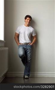 Young adult man leaning against white wall, wearing a white t-shirt.
