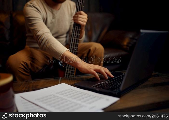 Young adult man learning playing guitar through internet. Online music course, music video tutorial. Young man learning playing guitar through internet