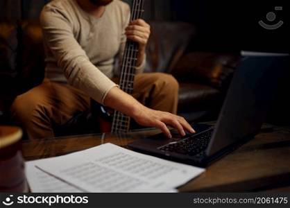 Young adult man learning playing guitar through internet. Online music course, music video tutorial. Young man learning playing guitar through internet