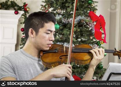 Young adult man playing the violin with Christmas tree in background