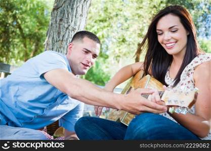 Young Adult Man Teaching Girlfriend How To Play The Guitar Outside in the Park.