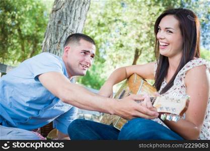 Young Adult Man Teaching Girlfriend How To Play The Guitar Outside in the Park.