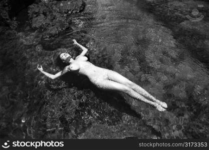 Young adult nude Caucasian woman floating in tidal pool in Maui.