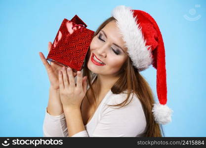 Young adult pretty woman is happy to give Christmas gifts. Female wearing red Santa Claus hat holding presents. Blue background. Happy Christmas woman receiving gifts