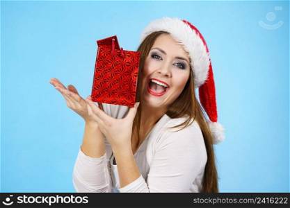 Young adult pretty woman is happy to give Christmas gifts. Female wearing red Santa Claus hat holding presents. Blue background. Happy Christmas woman receiving gifts