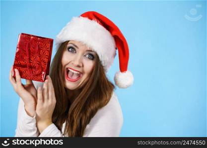 Young adult pretty woman is happy to give Christmas gifts. Female wearing red Santa Claus hat holding presents. Blue background. Happy Christmas woman receiving gifts