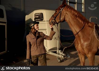 Young adult smiling rider woman stroking harnessed horse nose showing love and care. Friendship equine concept. Young adult smiling rider woman stroking horse nose