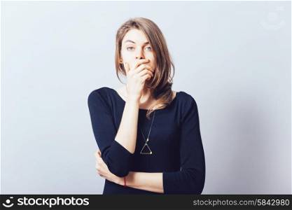 young adult woman holding hand over her mouth over grey background
