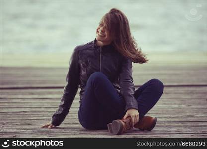Young adult woman sitting on a wooden jetty on the river
