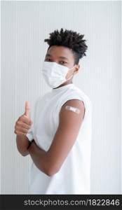 Young African American boy wear face mask smile and showing plaster stuck on arm to show that man get vaccinated with thumb up hand. White background