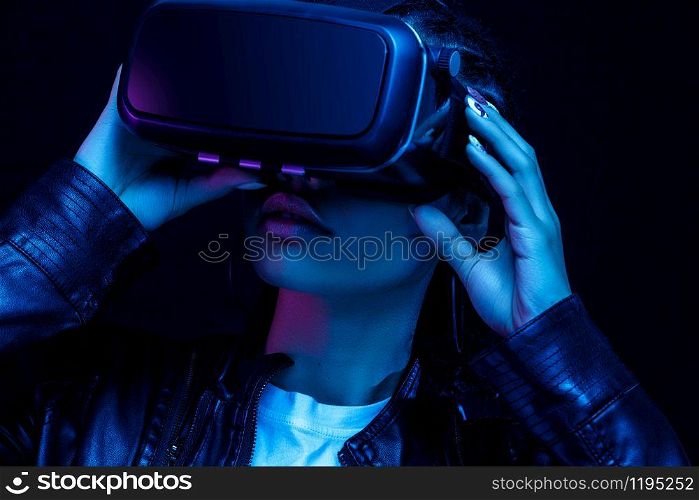 Young african american girl playing game using VR glasses, enjoying 360 degree virtual reality headset for gaming, isolated on black background in neon light