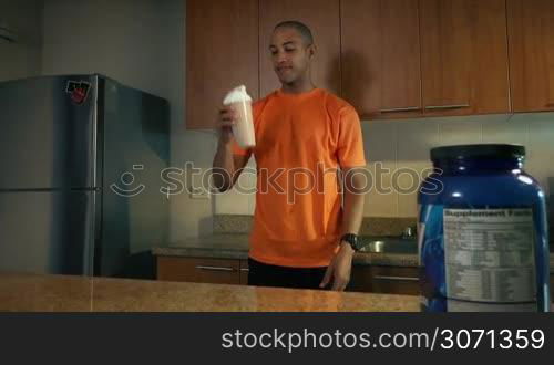 Young african american man in domestic kitchen, drinking a milk shake with proteins and vitamins. The guy tastes the beverage and smiles