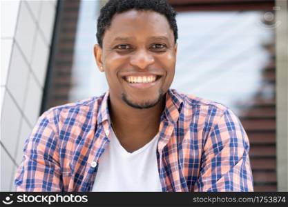 Young african american man looking at the camera while sitting at a store window on the street. Urban concept.