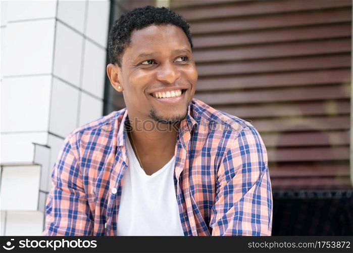 Young african american man relaxed and enjoying while sitting at a store window on the street.