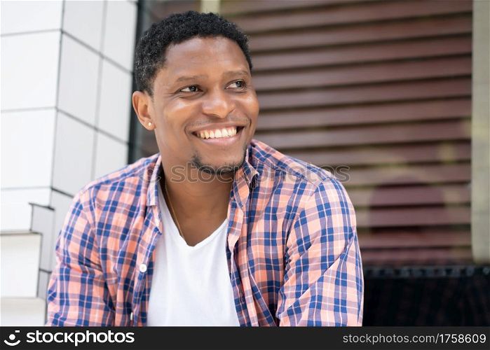 Young african american man relaxed and enjoying while sitting at a store window on the street.
