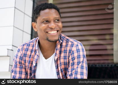 Young african american man relaxed and enjoying while sitting at a store window on the street.