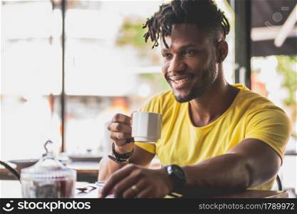 Young African American man relaxing while drinking a cup of coffee at a coffee shop.