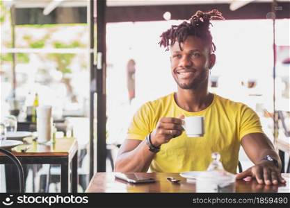 Young African American man relaxing while drinking a cup of coffee at a coffee shop.