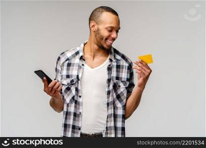 Young african-american man smiling and hoding credit card and mobile cell phone over grey background with copy space.. Young african-american man smiling and hoding credit card and mobile cell phone over grey background with copy space