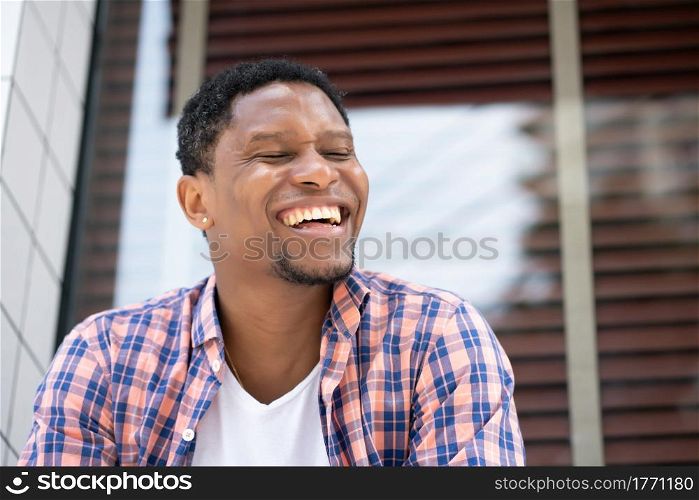 Young african american man smiling while sitting at a store window on the street. Urban concept.