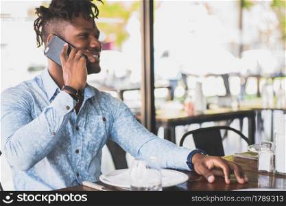 Young african american man talking on the phone while sitting in a restaurant.