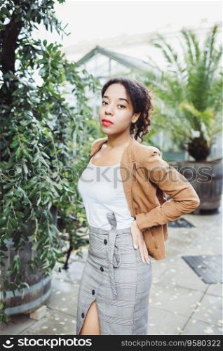 Young African American mixed race woman in brown jacket in park or street outdoor. Fall or spring season. Young African American mixed race woman in park. Fall or spring season