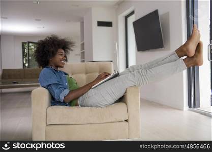 Young african american woman at home in the chair relaxing in her luxury lliving room reading laptop PC surf internet and work