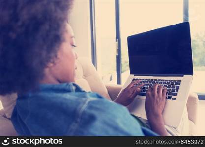 Young african american woman at home in the chair relaxing in her luxury lliving room reading laptop PC surf internet and work