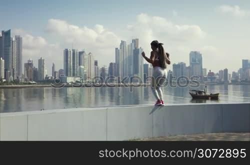 Young african american woman in sports clothing, exercising early morning in the city and jumping for joy at the end of her daily workout. Buildings and urban skyline in background. Slowmotion 120p