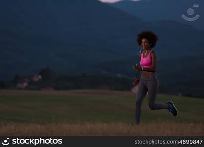 young African american woman runner with headphones jogging outdoors in nature beautiful summer night - Fitness, people and healthy lifestyle