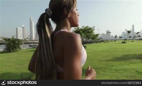 Young african american woman running and exercising early morning in the city, training along the Cinta Costera in Panama. Steadicam shot