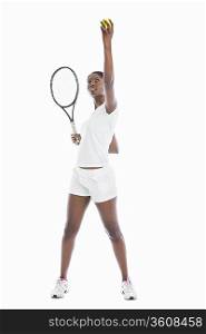 Young African American woman serving tennis ball against white background