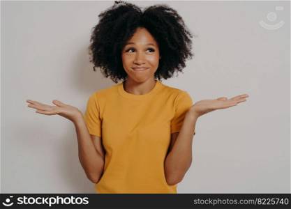 Young african american woman standing in casual clothes with clueless and funny confused expression with arms and hands raised, isolated over white studio background. Positive body language concept. Young african woman standing with clueless and funny confused expression with arms and hands raised