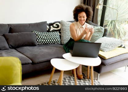 Young african american woman web-surfing internet and sitting on sofa