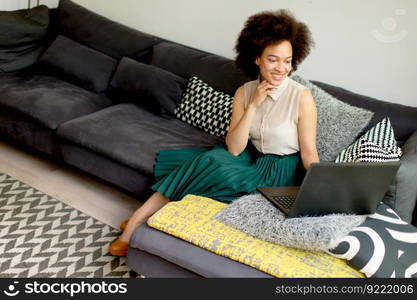 Young african american woman web-surfing internet and sitting on sofa