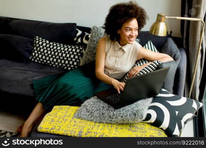 Young african american woman web-surfing internet and sitting on sofa