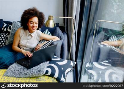 Young african american woman web-surfing internet and sitting on sofa