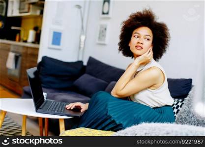 Young african american woman with laptop computer sitting in bright living room at home