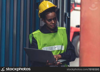 Young African American woman worker at overseas shipping container yard . Logistics supply chain management and international goods export concept .. Young African American woman worker at overseas shipping container yard