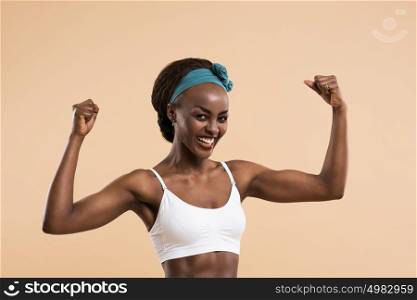Young african athletic girl posing and showing muscles on a beige background