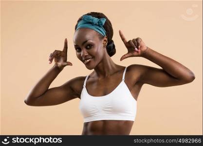Young african athletic girl posing and showing muscles on a beige background