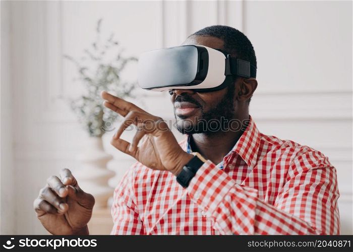 Young african businessman wearing VR glasses touching 3d objects in air with hands while playing games or watching video in digital world, interacting with interface in virtual reality at work. Young african businessman wearing VR glasses touching 3d objects, interacting with virtual reality