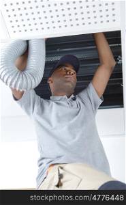 young african male electrician on stepladder fitting ventilation