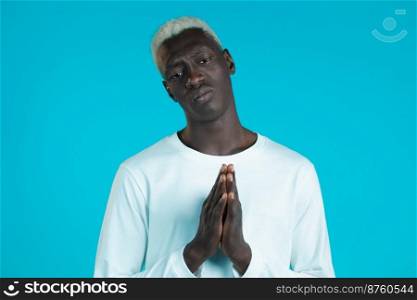 Young african man in white long sleeve praying over blue background. Guy begging someone satisfy his desires, help with. Young african man in white long sleeve praying over blue background. Guy begging someone satisfy his desires, help with.