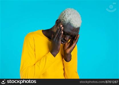 Young african man in yellow having headache, studio portrait. Guy putting hands on head, isolated on blue background. Concept of problems, medicine, illness.. Young african man in yellow having headache, studio portrait. Guy putting hands on head, isolated on blue background. Concept of problems, medicine, illness