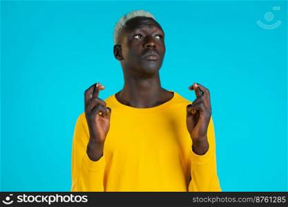 Young african man in yellow long sleeve praying over blue background. Guy begging someone satisfy his desires, help with. Young african man in yellow long sleeve praying over blue background. Guy begging someone satisfy his desires, help with.