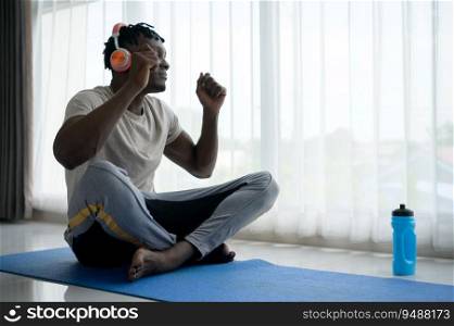 Young African man relaxing, listening to music after finishing yoga exercise in the living room of the house