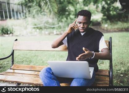 Young African man talking on phone disputing over computer, stressed, unsatisfied. Disappointed, confused, angry male arguing with technical online support or customer service. Bad connection concept. Young African man talking on phone disputing over computer, stressed, unsatisfied