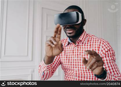 Young african man wearing VR glasses enjoying gaming experience at home, dark-skinned businessman in 3d goggles using innovative virtual reality technology in business while standing in modern office. Young african man wearing VR glasses enjoying gaming experience at home