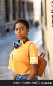 Young African woman wearing casual clothes and headphones looking at camera in urban background. Lifestyle Concept.. Young African woman wearing casual clothes and headphones looking at camera